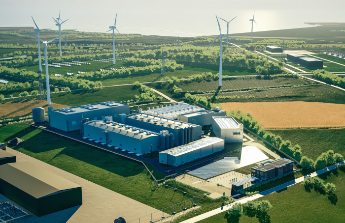 Windräder und ein Elektrolyseur stehen zwischen grünen Feldern und Wiesen.